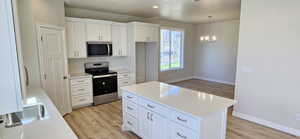 Kitchen featuring a notable chandelier, appliances with stainless steel finishes, light countertops, light wood-style flooring, and white cabinetry