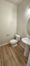 Half bath with toilet, baseboards, a sink, and wood finished floors