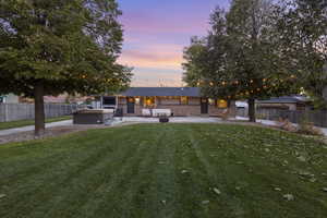 Back of property with a patio area, a hot tub, a fenced backyard, and a yard