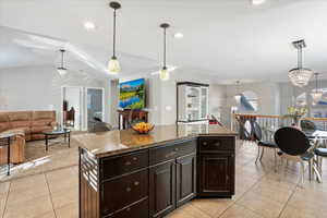 Kitchen with light tile patterned floors, open floor plan, a center island, dark stone countertops, and decorative light fixtures