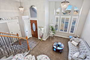 Carpeted entryway featuring baseboards, a towering ceiling, and a notable chandelier