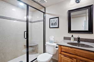 Bathroom with a shower stall, visible vents, vanity, and toilet