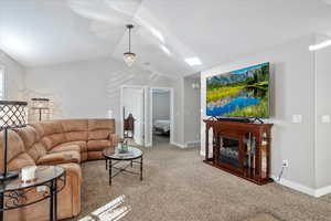 Living room featuring baseboards, visible vents, a glass covered fireplace, lofted ceiling, and carpet flooring