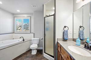 Bathroom featuring a garden tub, toilet, vanity, visible vents, and a stall shower