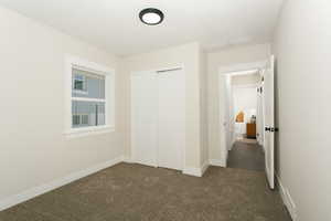 Unfurnished bedroom with dark colored carpet, a closet, and baseboards