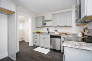 Kitchen with dark wood-style floors, light stone counters, gray cabinetry, a sink, and dishwasher