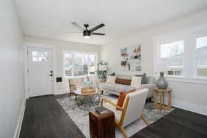 Living area with dark wood-style floors, a ceiling fan, and baseboards