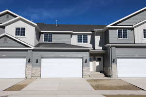 Townhome / multi-family property with a garage, driveway, board and batten siding, and stone siding