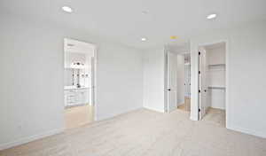 Unfurnished bedroom with recessed lighting, light carpet, baseboards, a closet, and a walk in closet