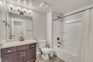 Full bathroom with shower / bath combination with curtain, toilet, vanity, a textured ceiling, and wood finished floors