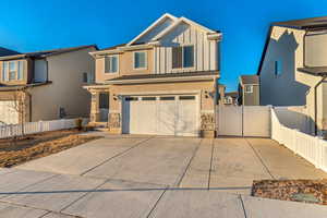 View of front of home with a garage, fence, stone siding, a gate, and board and batten siding