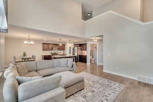 Living room featuring a notable chandelier, visible vents, a towering ceiling, light wood-style floors, and baseboards