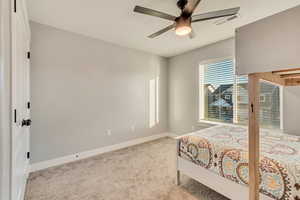 Carpeted bedroom with baseboards, visible vents, and a ceiling fan