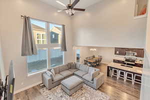 Living room featuring baseboards, a high ceiling, ceiling fan with notable chandelier, and light wood-style floors