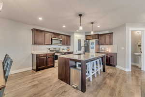 Kitchen with a breakfast bar area, appliances with stainless steel finishes, dark brown cabinets, light wood-type flooring, and a sink