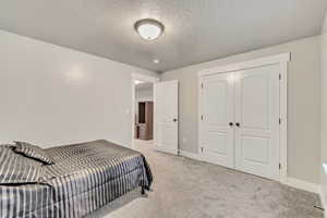 Bedroom featuring a textured ceiling, baseboards, a closet, and light colored carpet