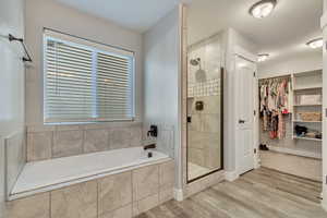 Full bath featuring a stall shower, a walk in closet, a bath, and wood finished floors