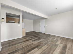 Unfurnished living room with dark wood-style floors, beamed ceiling, and baseboards