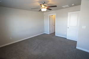 Unfurnished room with a ceiling fan, dark colored carpet, visible vents, and baseboards