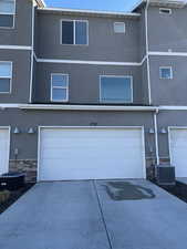 Exterior space with a garage, stone siding, driveway, and central air condition unit