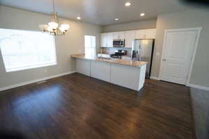 Kitchen featuring white cabinets, light stone counters, dark wood-style flooring, a peninsula, and stainless steel appliances