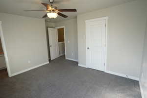 Unfurnished bedroom with ceiling fan, baseboards, and dark colored carpet