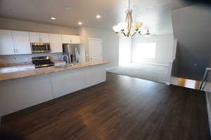 Kitchen featuring a sink, white cabinetry, appliances with stainless steel finishes, light stone countertops, and dark wood finished floors