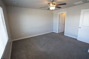 Unfurnished room with ceiling fan, dark carpet, visible vents, and baseboards