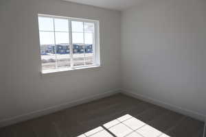 Empty room with a residential view, baseboards, dark colored carpet, and a wealth of natural light