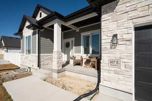 Property entrance with covered porch, stone siding, and a shingled roof