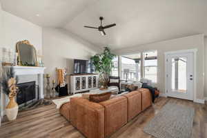 Living room featuring a brick fireplace, ceiling fan, vaulted ceiling, and wood finished floors