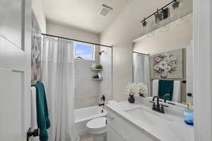 Full bath featuring toilet, shower / bath combo with shower curtain, vanity, and visible vents