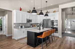 Kitchen with tasteful backsplash, appliances with stainless steel finishes, wood finished floors, light countertops, and a sink