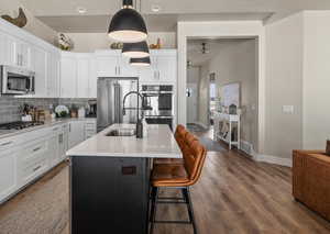 Kitchen featuring dark wood-style flooring, white cabinets, appliances with stainless steel finishes, backsplash, and an island with sink