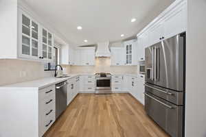 Kitchen with premium range hood, a sink, appliances with stainless steel finishes, light wood finished floors, and tasteful backsplash