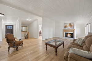 Living room featuring visible vents, ornamental molding, light wood-type flooring, wooden ceiling, and a lit fireplace