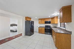 Kitchen with brown cabinets, light tile patterned floors, dark countertops, a sink, and black appliances