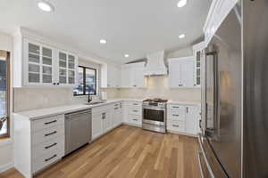 Kitchen featuring light wood-style flooring, a sink, white cabinetry, high quality appliances, and custom range hood