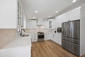 Kitchen with premium appliances, light wood finished floors, custom range hood, white cabinets, and a sink