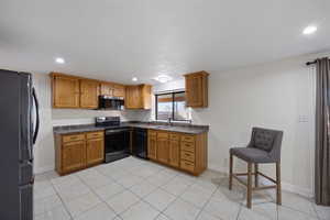 Kitchen with brown cabinetry, dark countertops, and black appliances