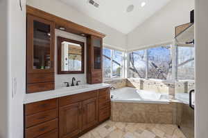 Full bathroom with stone tile floors, lofted ceiling, visible vents, vanity, and a bath