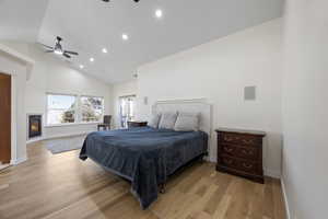 Bedroom with light wood-style floors, a warm lit fireplace, baseboards, and high vaulted ceiling