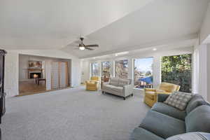 Living room with a warm lit fireplace, ceiling fan, carpet, vaulted ceiling, and recessed lighting