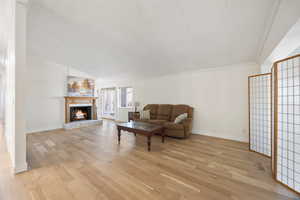 Living room featuring lofted ceiling, visible vents, light wood-style floors, ornamental molding, and a lit fireplace