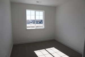 Spare room with dark colored carpet, visible vents, and baseboards