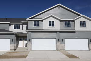 View of property featuring board and batten siding, concrete driveway, stone siding, and a garage