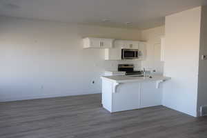 Kitchen featuring light countertops, appliances with stainless steel finishes, white cabinets, wood finished floors, and a peninsula