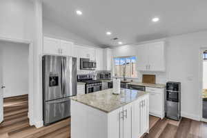 Kitchen with tasteful backsplash, lofted ceiling, appliances with stainless steel finishes, a kitchen island, and light stone countertops