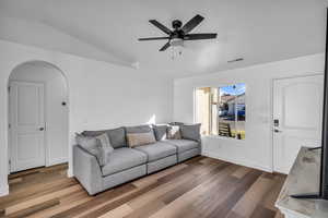 Living room featuring arched walkways, wood finished floors, visible vents, a ceiling fan, and vaulted ceiling