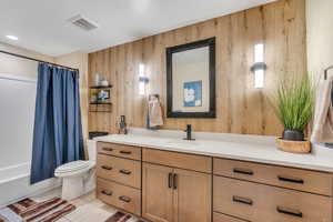 Full bathroom with wooden walls, visible vents, toilet, tile patterned flooring, and vanity